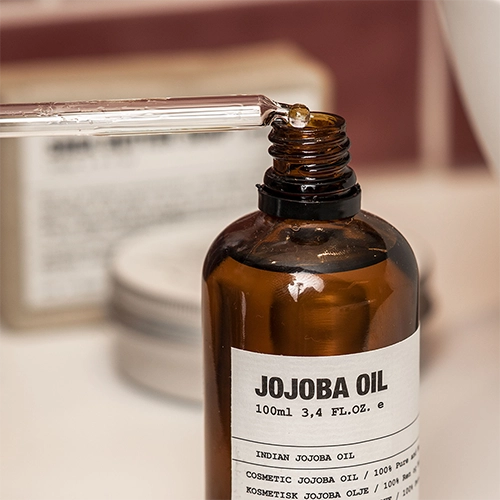 Pipet met jojoba olie rust op de rand van een geopende fles.