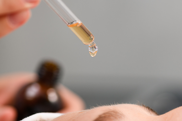 Nahaufnahme eines glänzenden Tropfens Gesichtsserum, der aus einer Pipette fällt oder auf der Haut liegt.