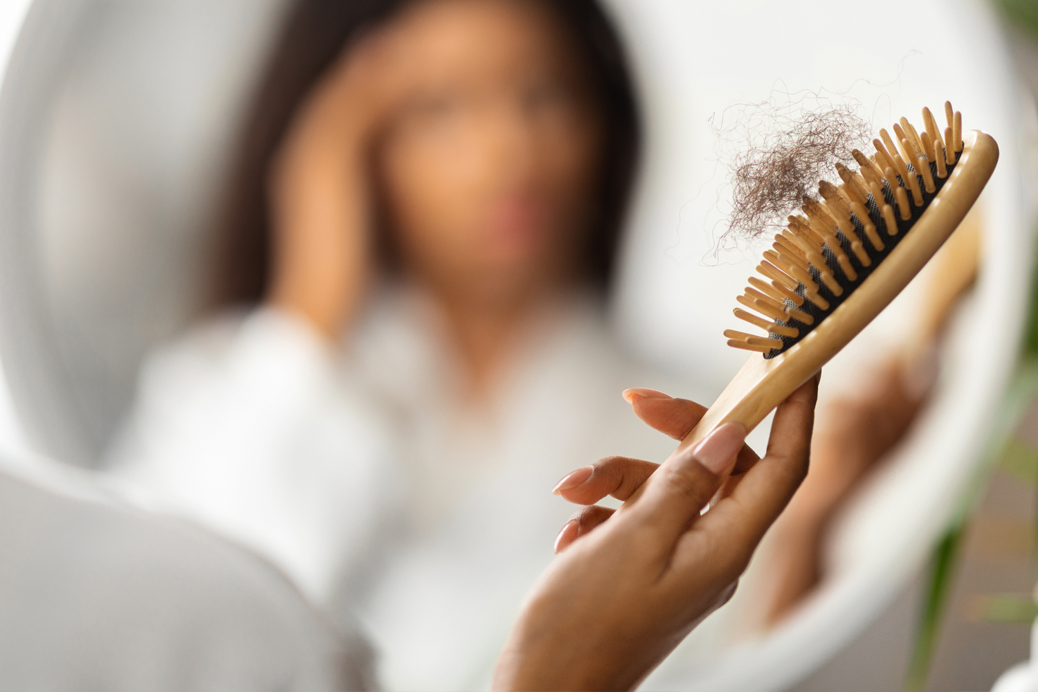 Frau kämmt Haar vor dem Spiegel mit Haarausfall