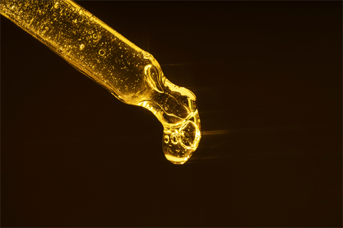 Een pipet gevuld met goudkleurige arganolie, waaruit een stralende druppel lijkt te vallen